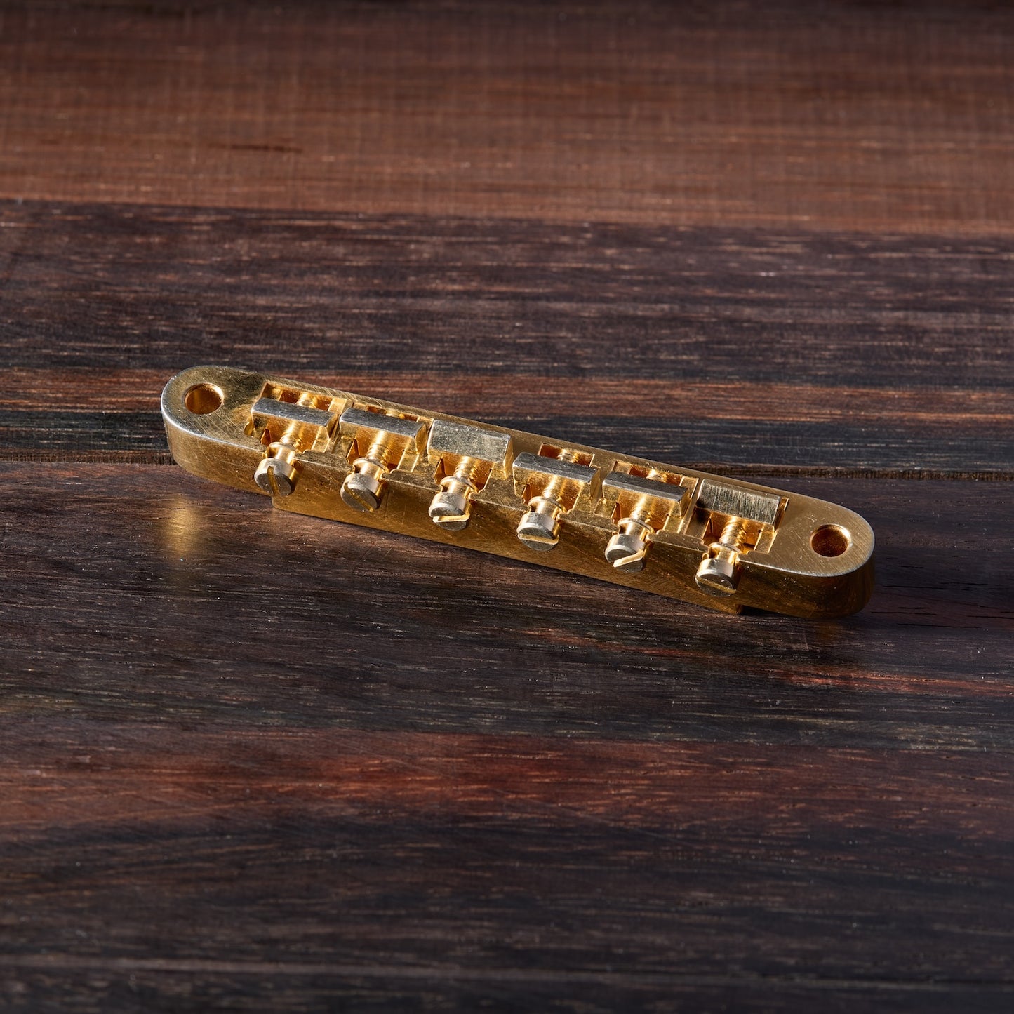 Gold Aged guitar bridge on a wooden surface