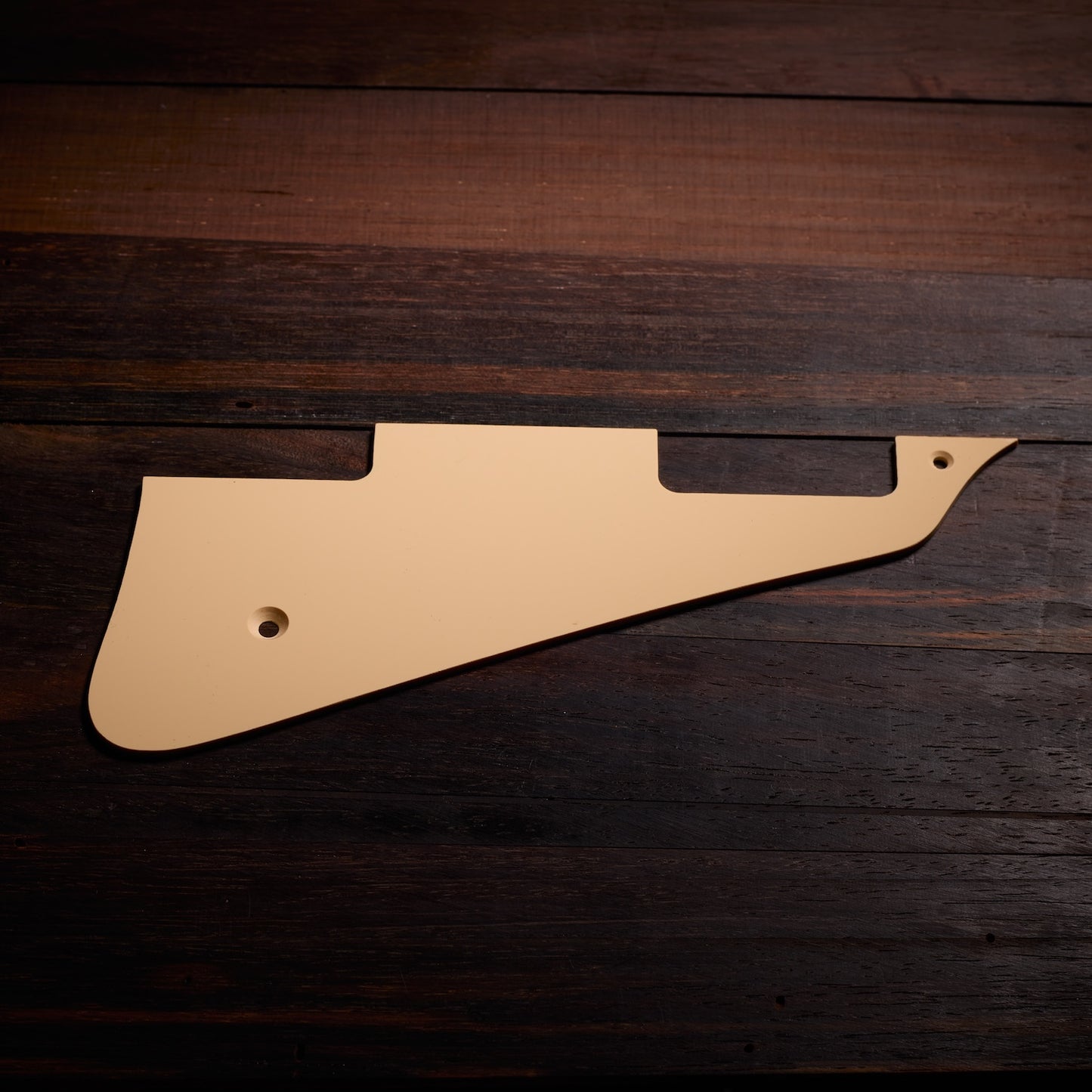 Beige guitar pickguard on a dark wooden surface