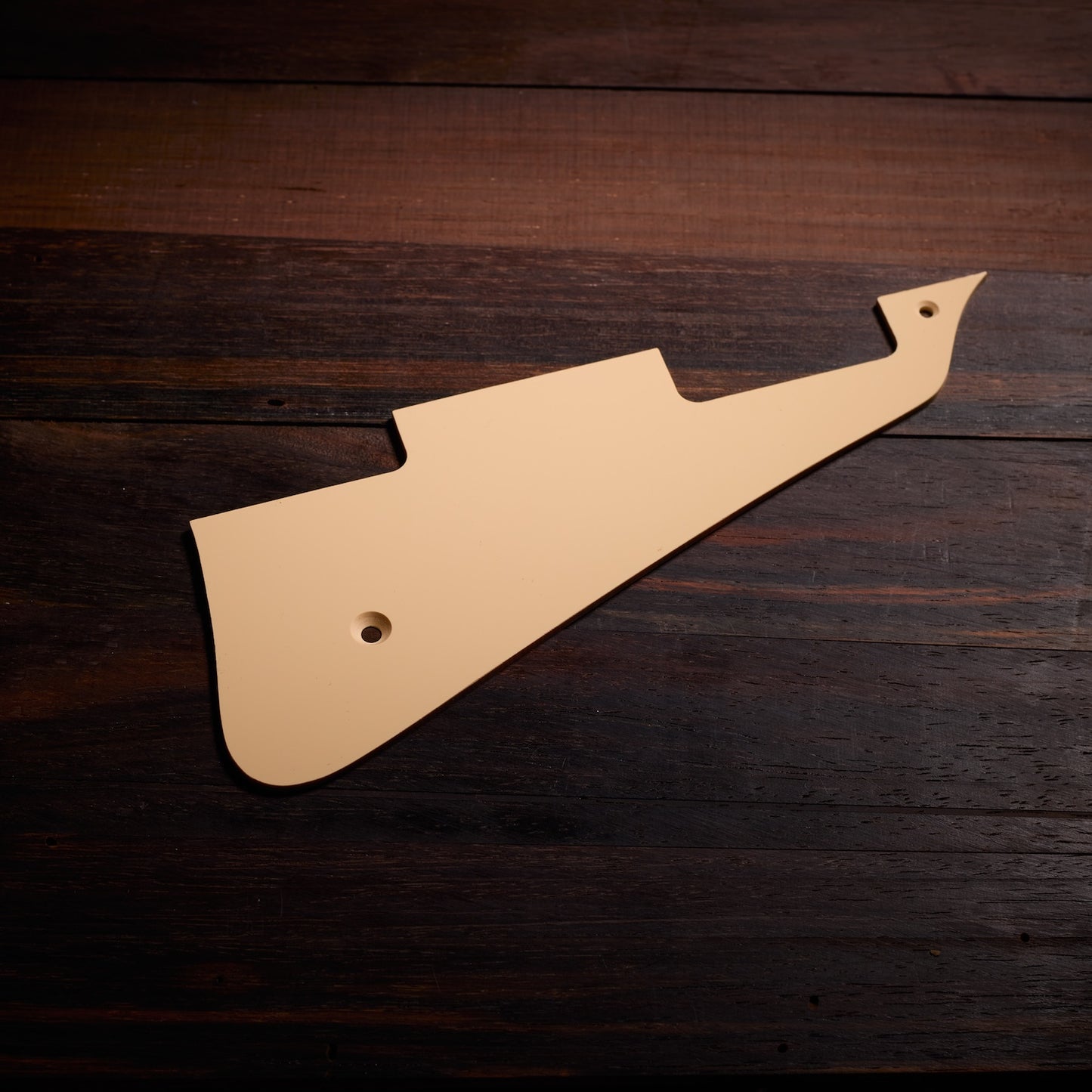 Beige guitar pickguard on a wooden surface